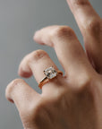 Asschercut diamond claw solitaire engagement ring with floral scroll side detailing, worn alone on a woman's finger.