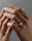Close-up of hands wearing multiple gold rings, including a thin Fairmined yellow gold wedding band with hand-engraved fern details.