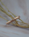 Starlight hammered rose gold wedding band ring with small round diamonds, resting on dried beige branches over a light gray marble surface.