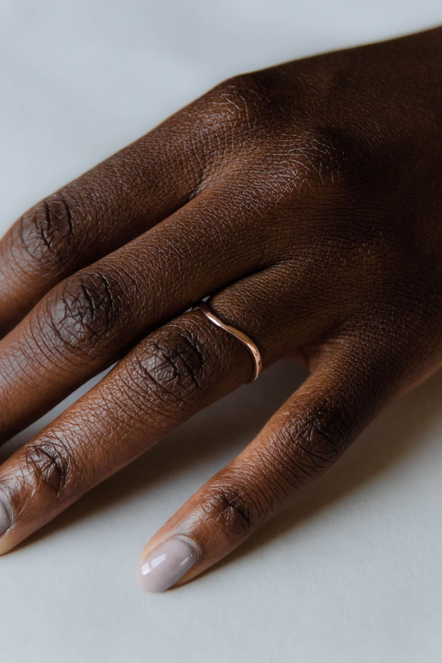 Close up of model hand wearing the curved Caia womens wedding band by Fluid Jewellery in yellow gold 3