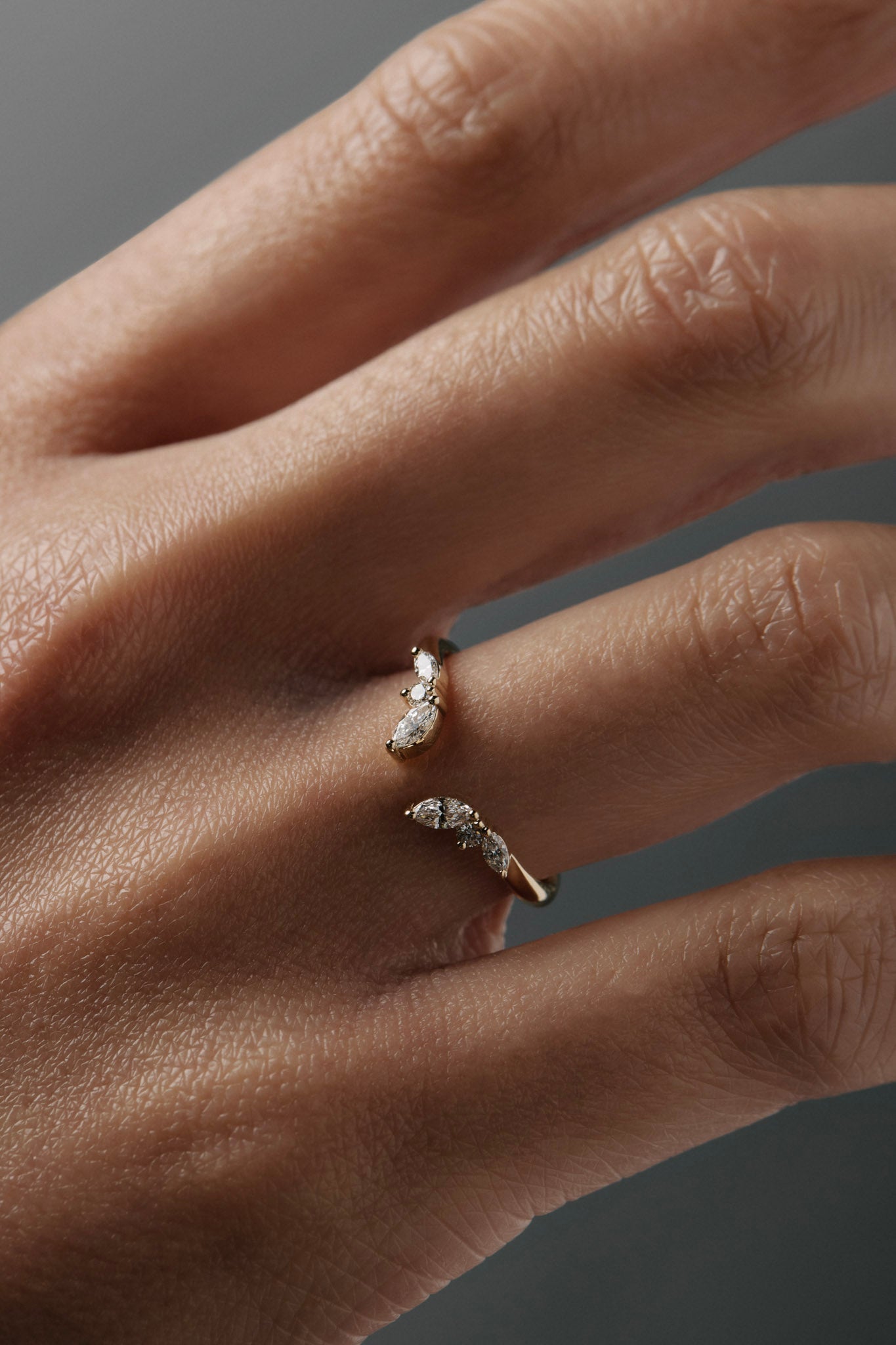 Close-up of a women's hand wearing the Aster open guard gold wedding band with marquise and round diamonds.