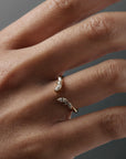Close-up of a women's hand wearing the Aster open guard gold wedding band with marquise and round diamonds.