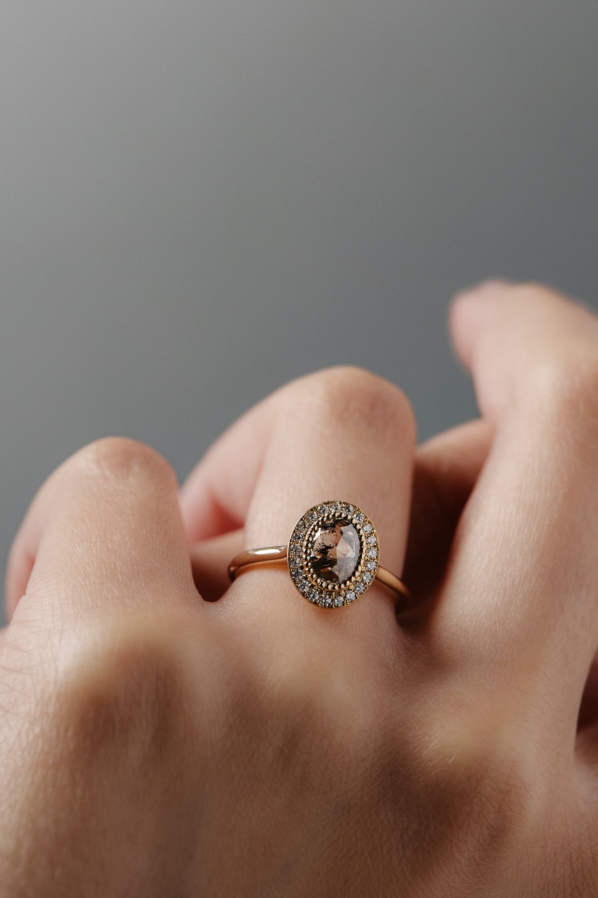 Close-up of a woman's hand wearing the Aura halo solitaire with a champagne toned Australian salt and pepper oval shaped rose cut diamond surrounded by Canadian diamonds. 