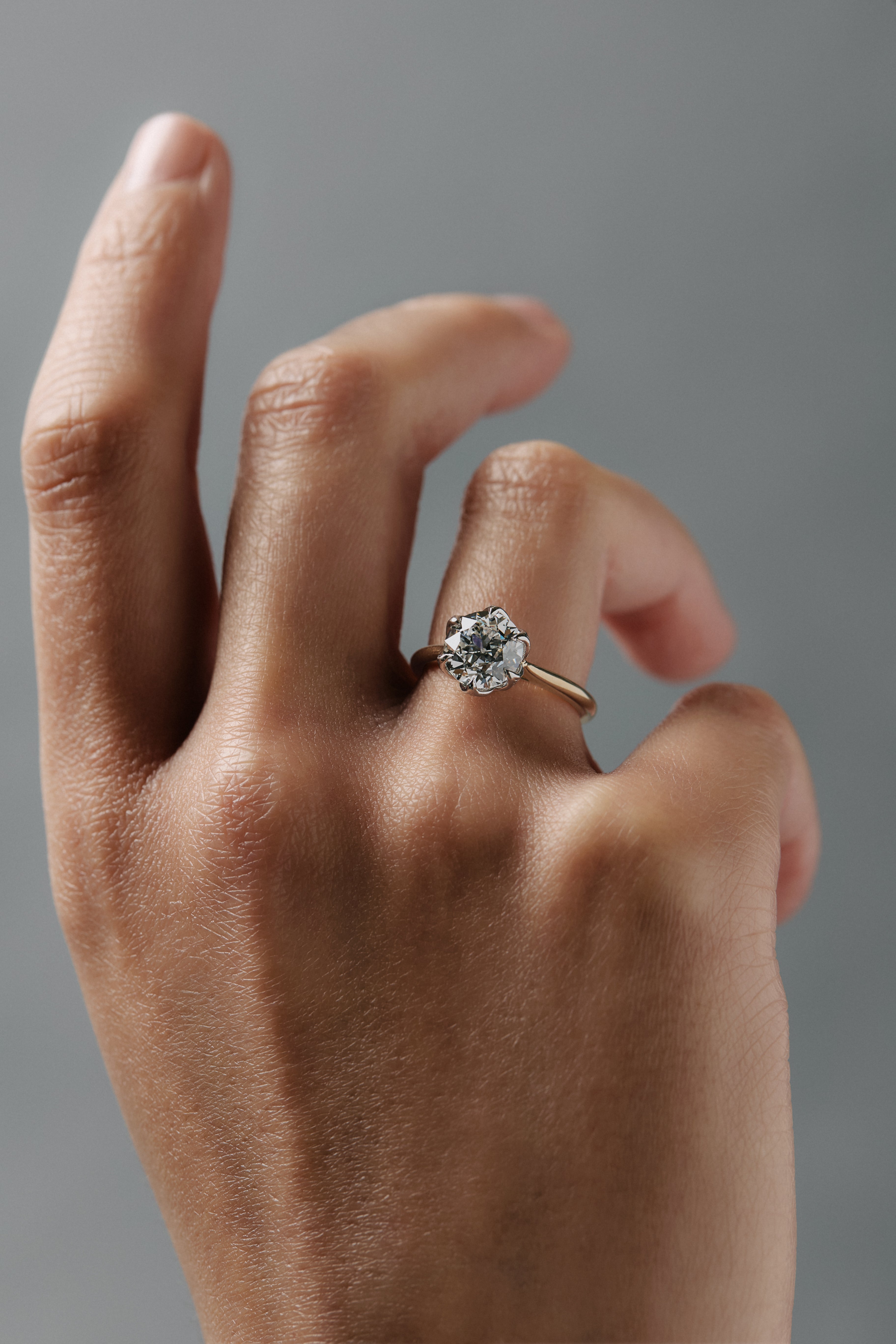 Close-up of a woman wearing the Cala tulip style solitaire with an antique floral filigree inspired platinum and gold setting and round Old European cut diamond. 