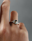 Close-up of the Celeste teal sapphire and Canadian diamond cluster engagement ring worn a woman's finger. 