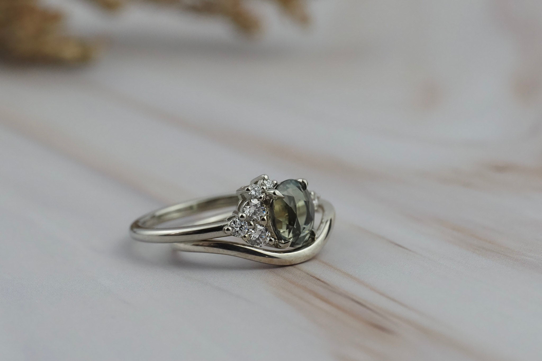 Close-up of the Celeste teal sapphire and diamond cluster engagement ring paired with a curved gold wedding band.