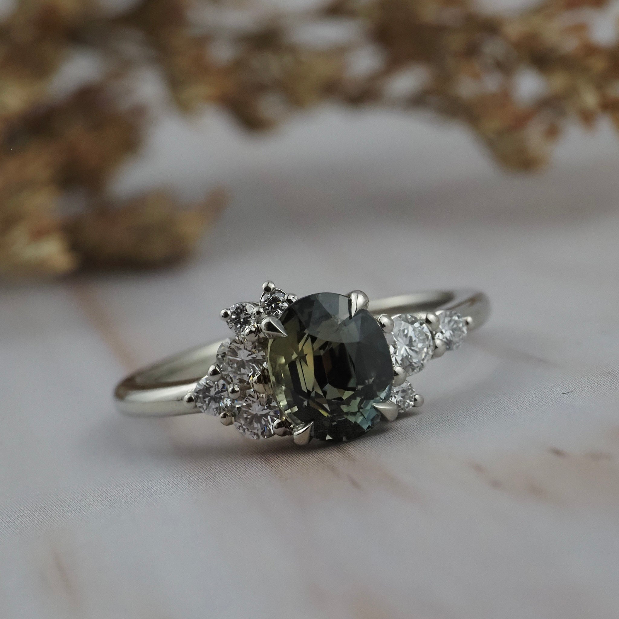 Celeste cluster engagement ring featuring a natural teal sapphire surrounded by diamonds crafted in a white gold setting.