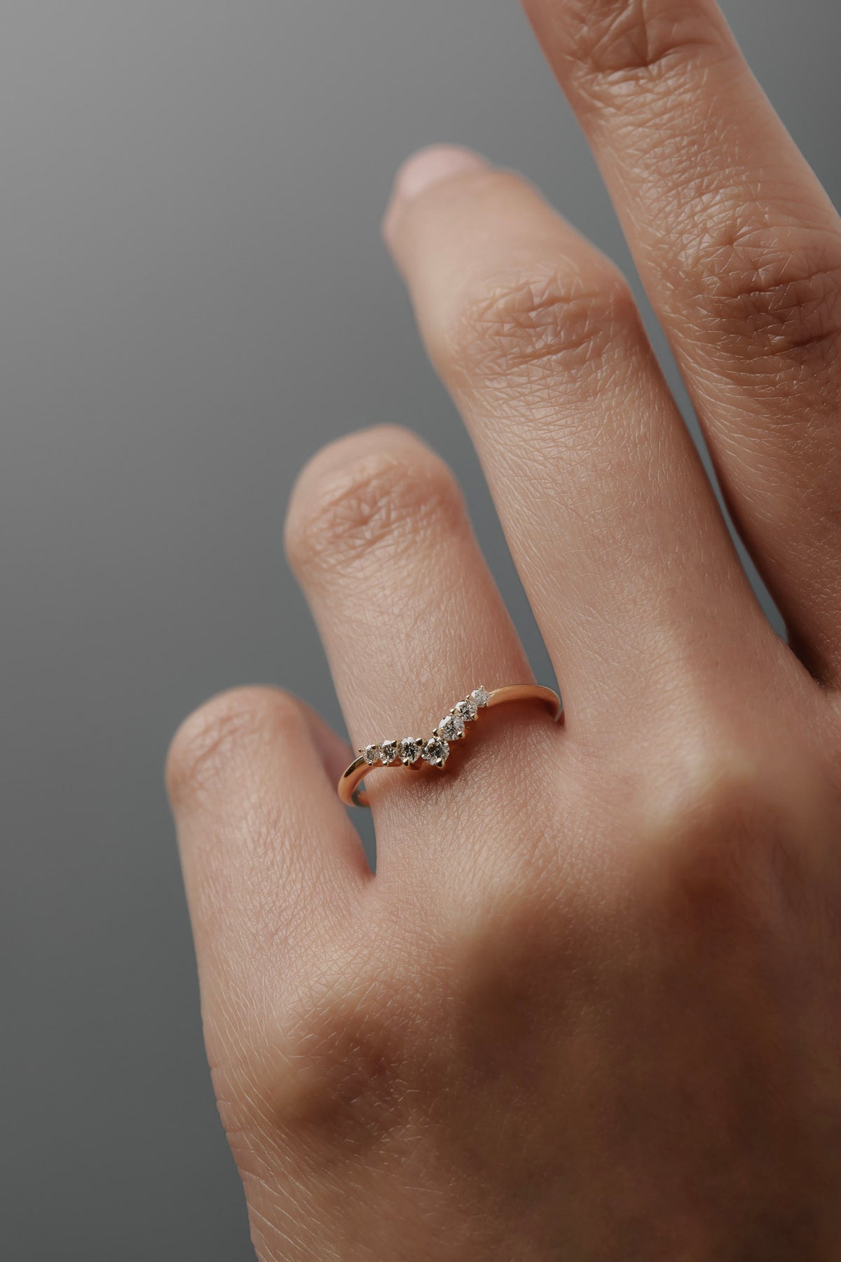 Close-up of the Claudia chevron wedding band in Fairmined gold with delicate diamonds worn on a woman's ring finger. 