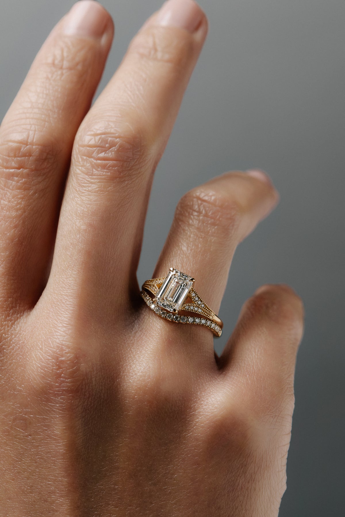 Cora split-shank milgrain emerald cut diamond solitaire paired with the Pernelle curved French pave diamond wedding band on a woman's finger.