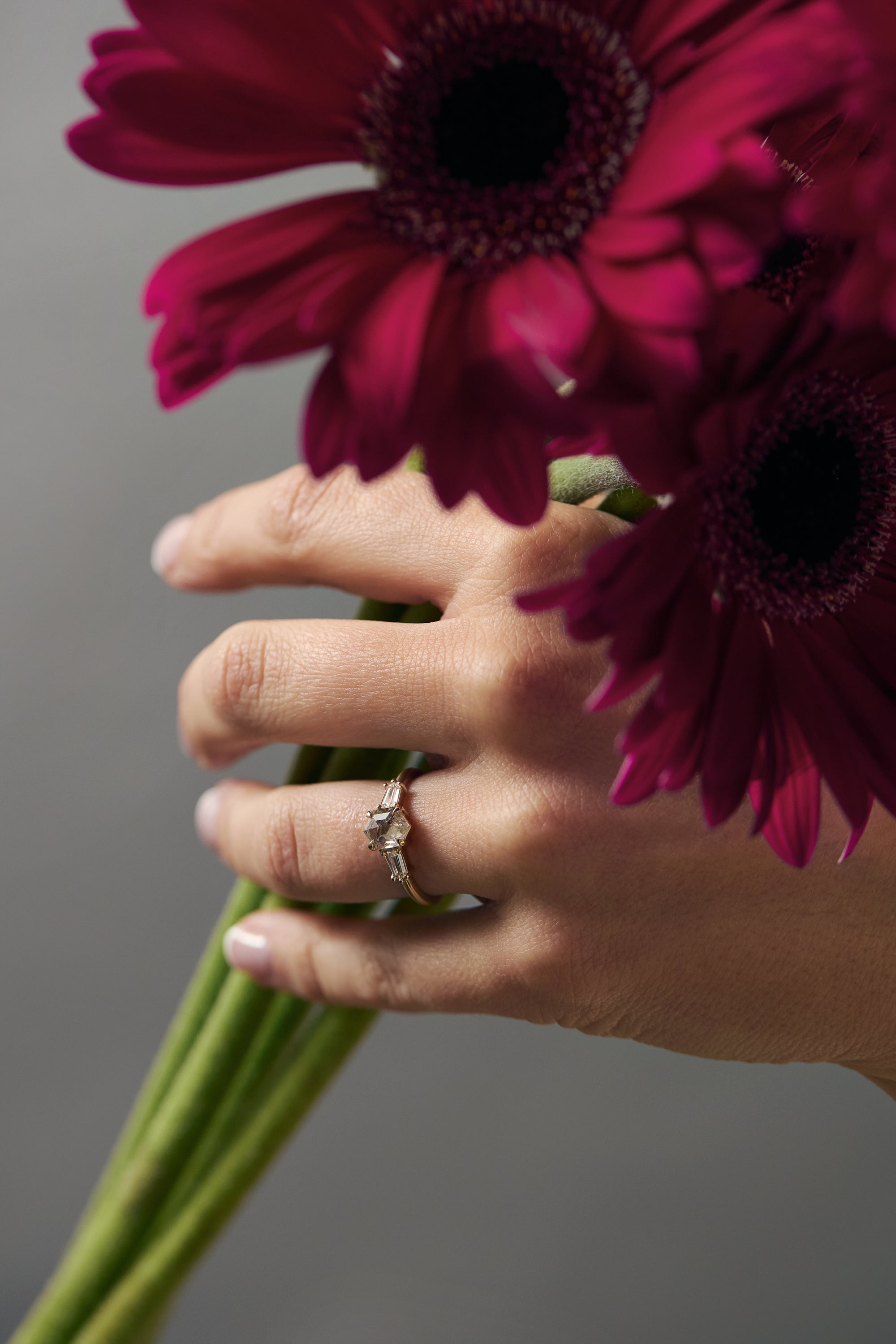 Esme hexagon-shaped- salt and pepper diamond engagement ring with tapered baguette diamonds worn on a woman's hand holding a flower.