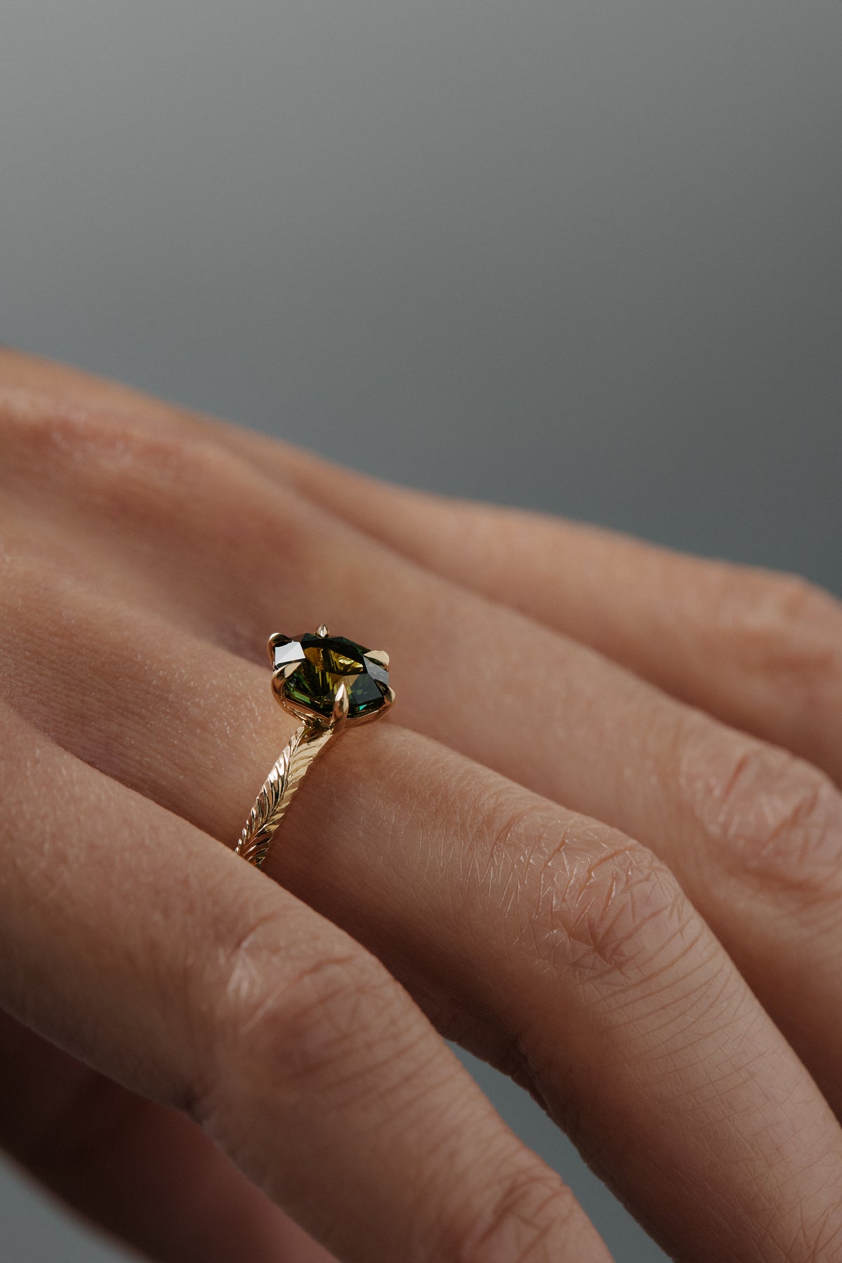 Close-up side view of the Fern hand-engraved green sapphire solitaire on a woman's hand, highlighting the detailed Fairmined gold band and setting.