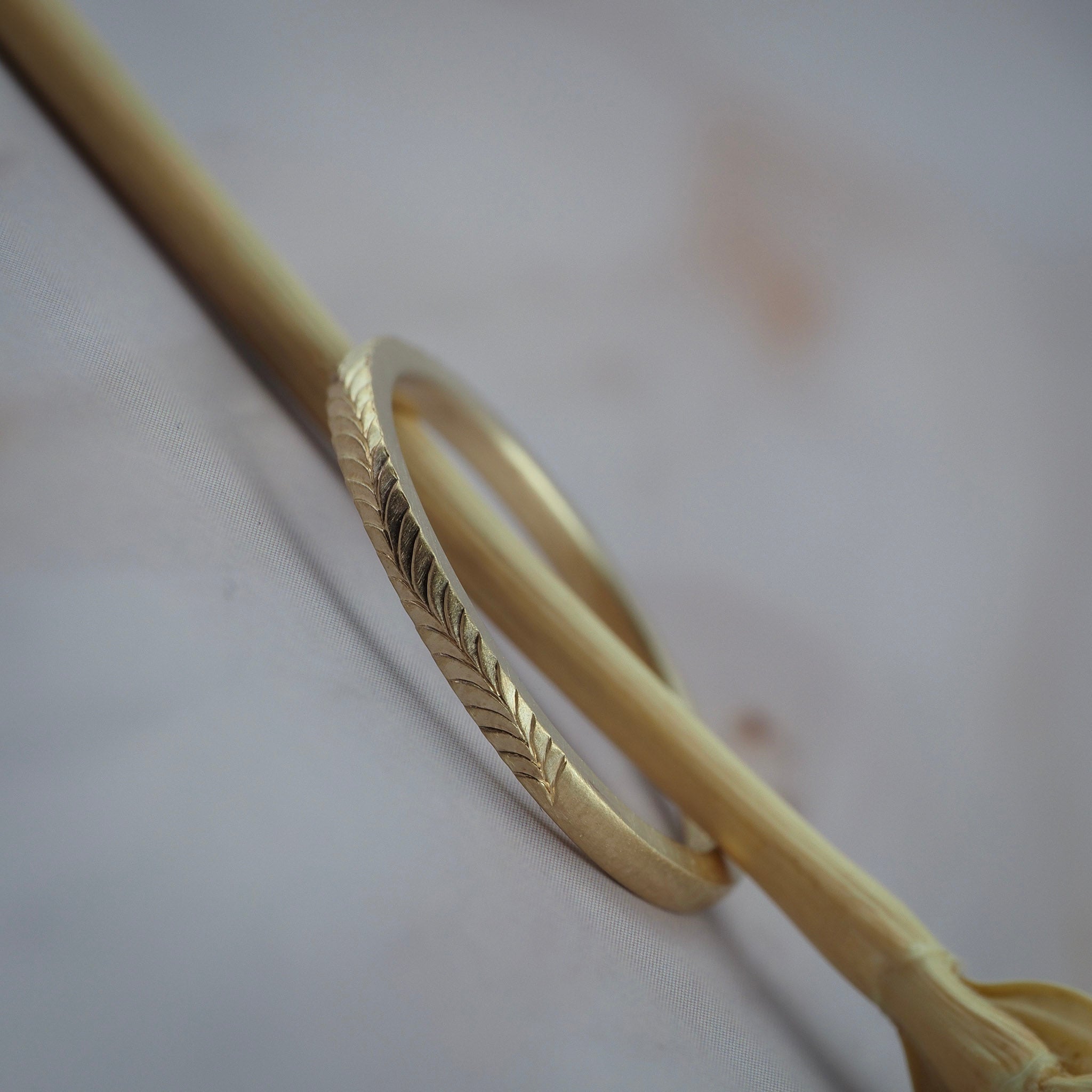 Close up side view of hand-engraved fern details on a thin Fairmined yellow gold wedding band.