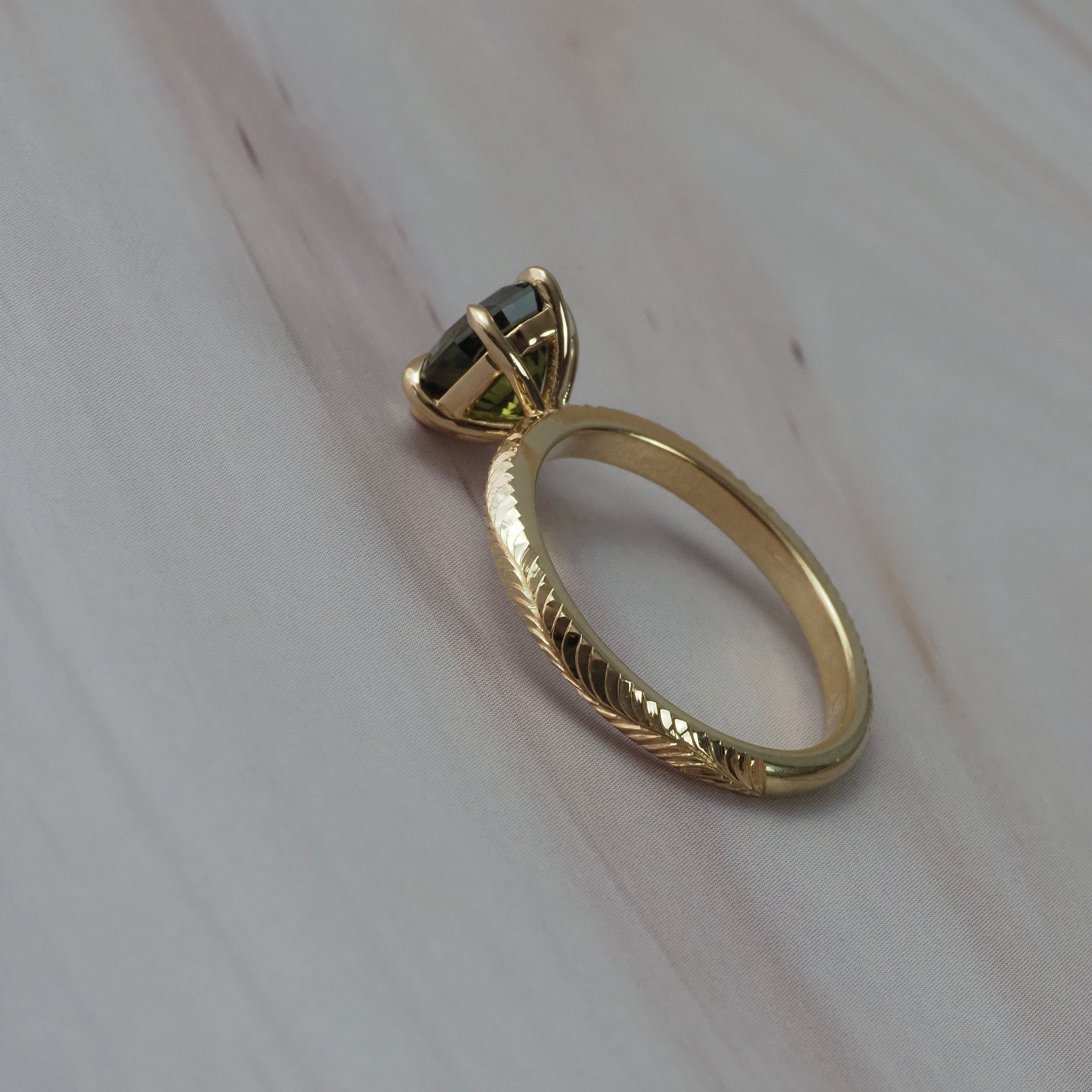 Back view of the Fern hand-engraved solitaire showing the detailed Fairmined gold band and setting around the step-cut oval green sapphire.