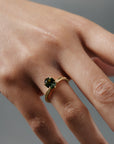 Close-up of a woman wearing the Fern hand engraved solitaire in Fairmined gold, featuring a step cut oval green sapphire.