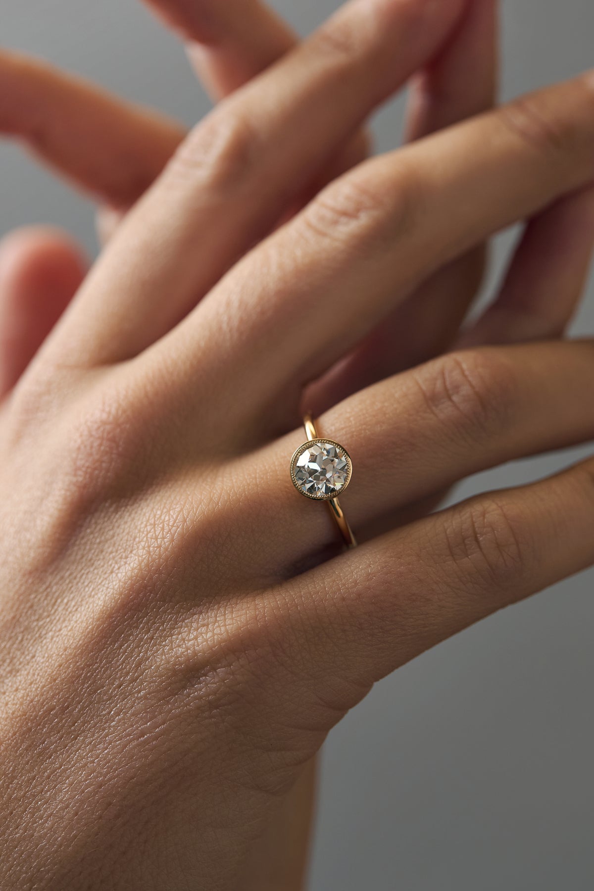 Close-up of the Flora gold milgrain bezel solitaire with an Old European cut diamond and floral side engravings worn on a woman's finger.