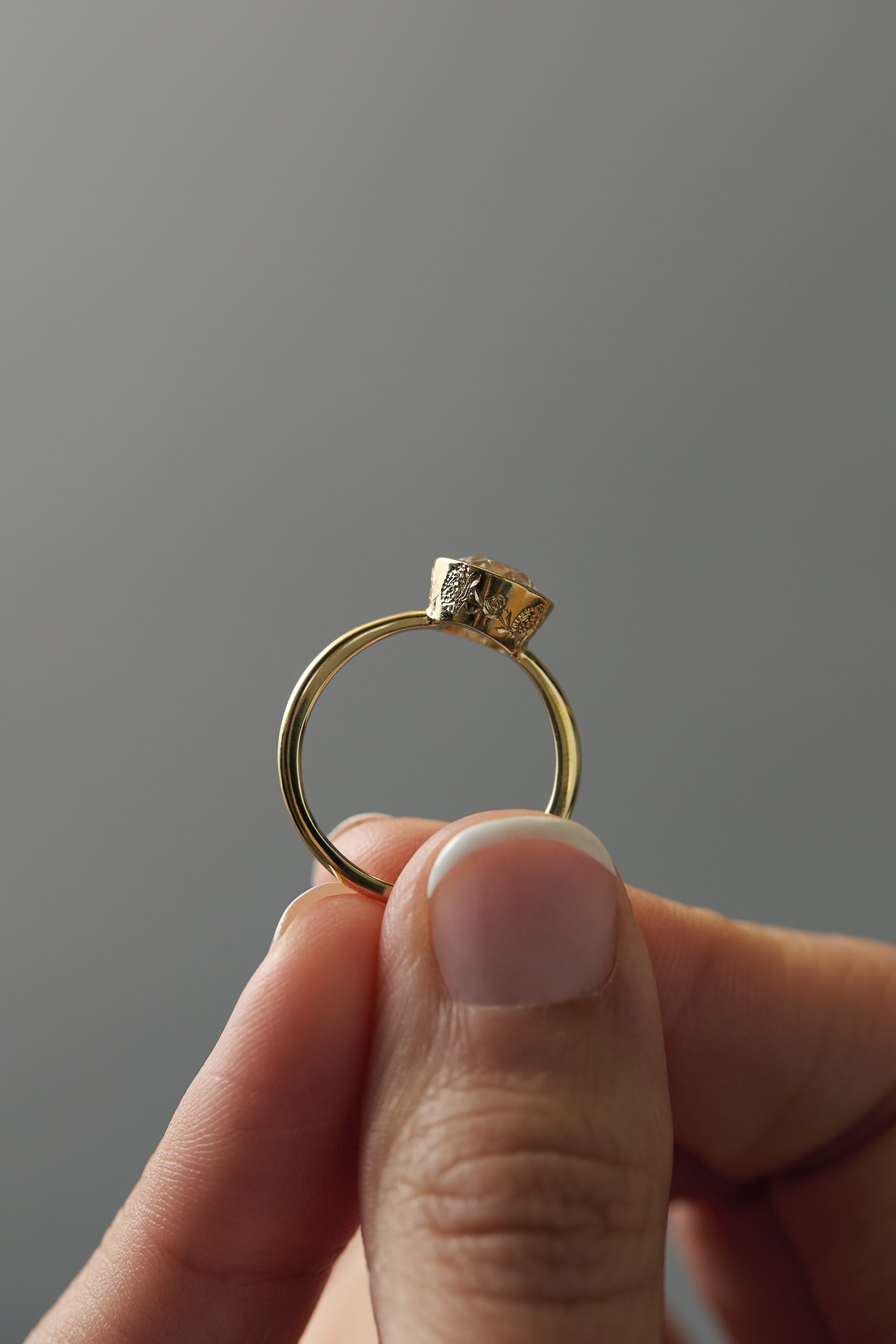Close-up side profile of the Flora gold solitaire showing the milgrain bezel and hand-engraved floral details.