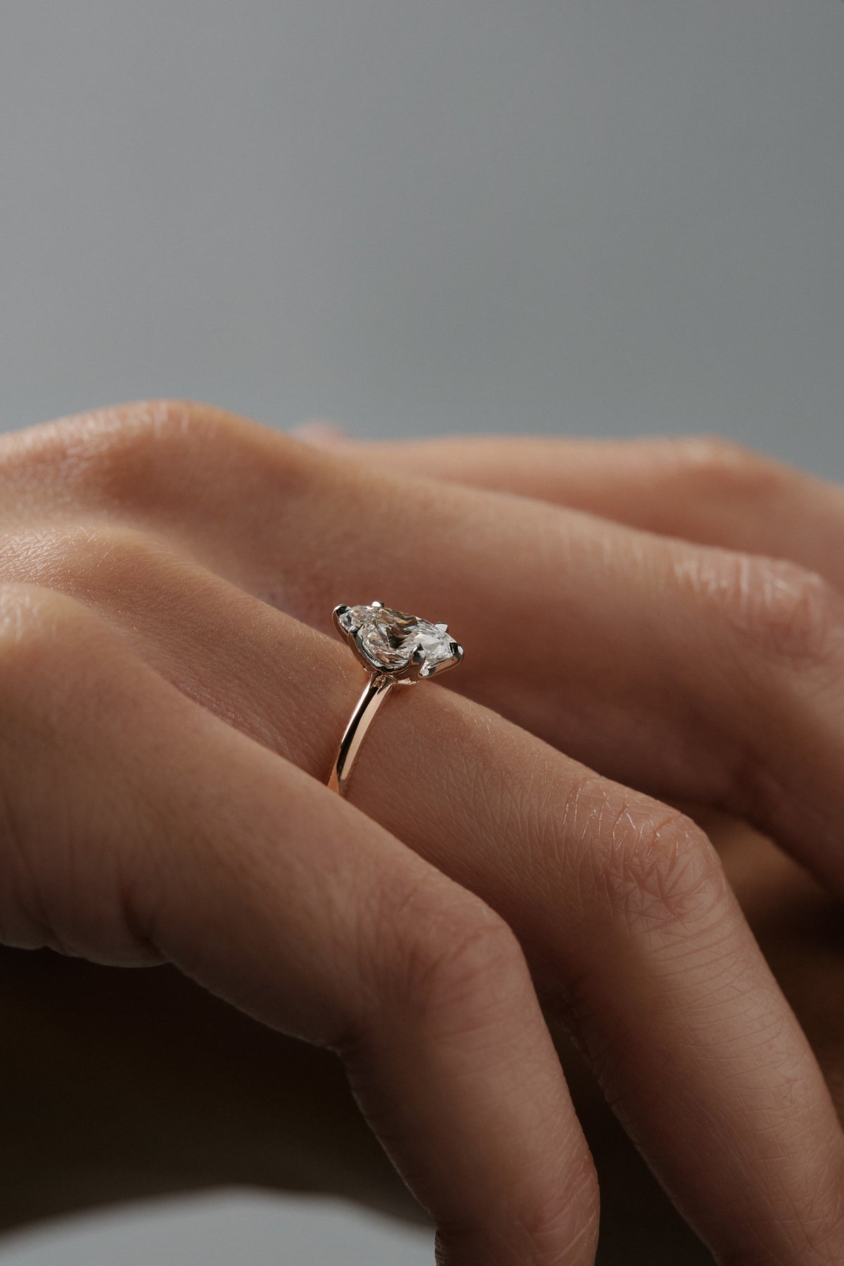 Close-up side profile of Lana six claw solitaire engagement ring worn on a woman's finger, showing the moval shaped antique cut Old European diamond  and two-tone platinum and rose gold setting.