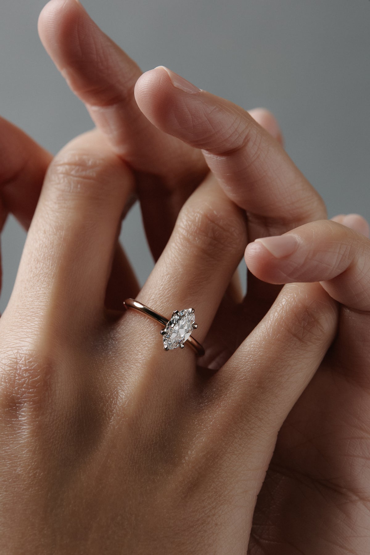 Stylized close-up of the Lena six claw solitaire engagement ring worn on a woman's finger, featuring a moral shaped antique cut Old European diamond in a two tone platinum and rose gold setting.