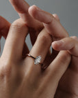 Stylized close-up of the Lena six claw solitaire engagement ring worn on a woman's finger, featuring a moral shaped antique cut Old European diamond in a two tone platinum and rose gold setting.