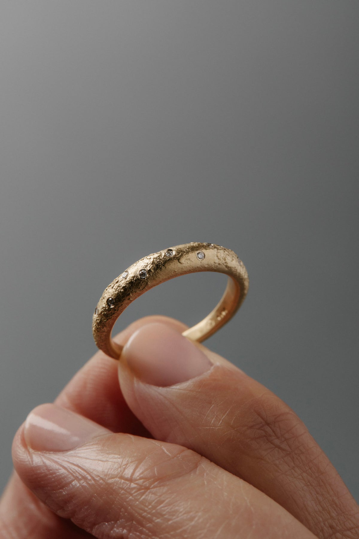 Close-up of women's hands holding the Luna textured yellow gold wedding band featuring small diamonds.