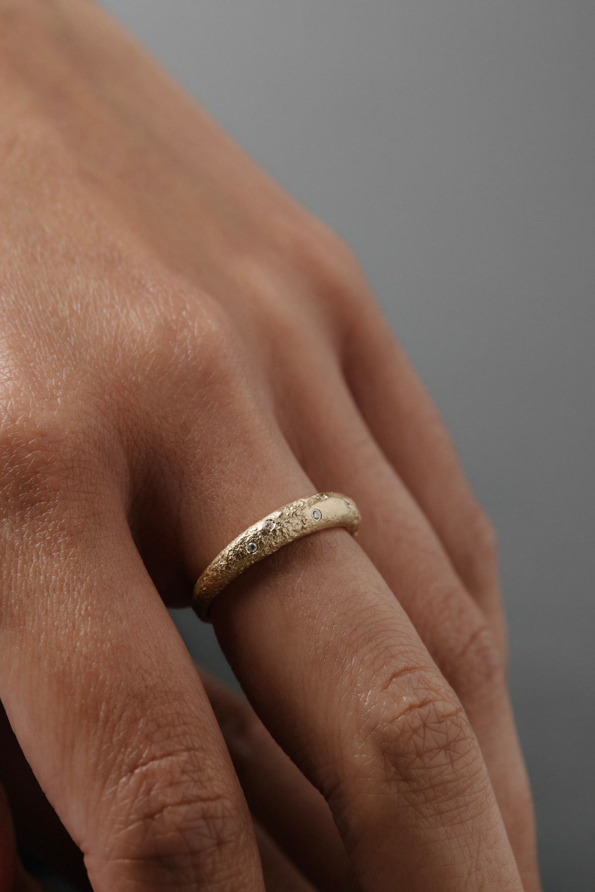 Close-up of a women wearing the Luna textured yellow gold wedding band with delicate Canadian diamonds on her finger.