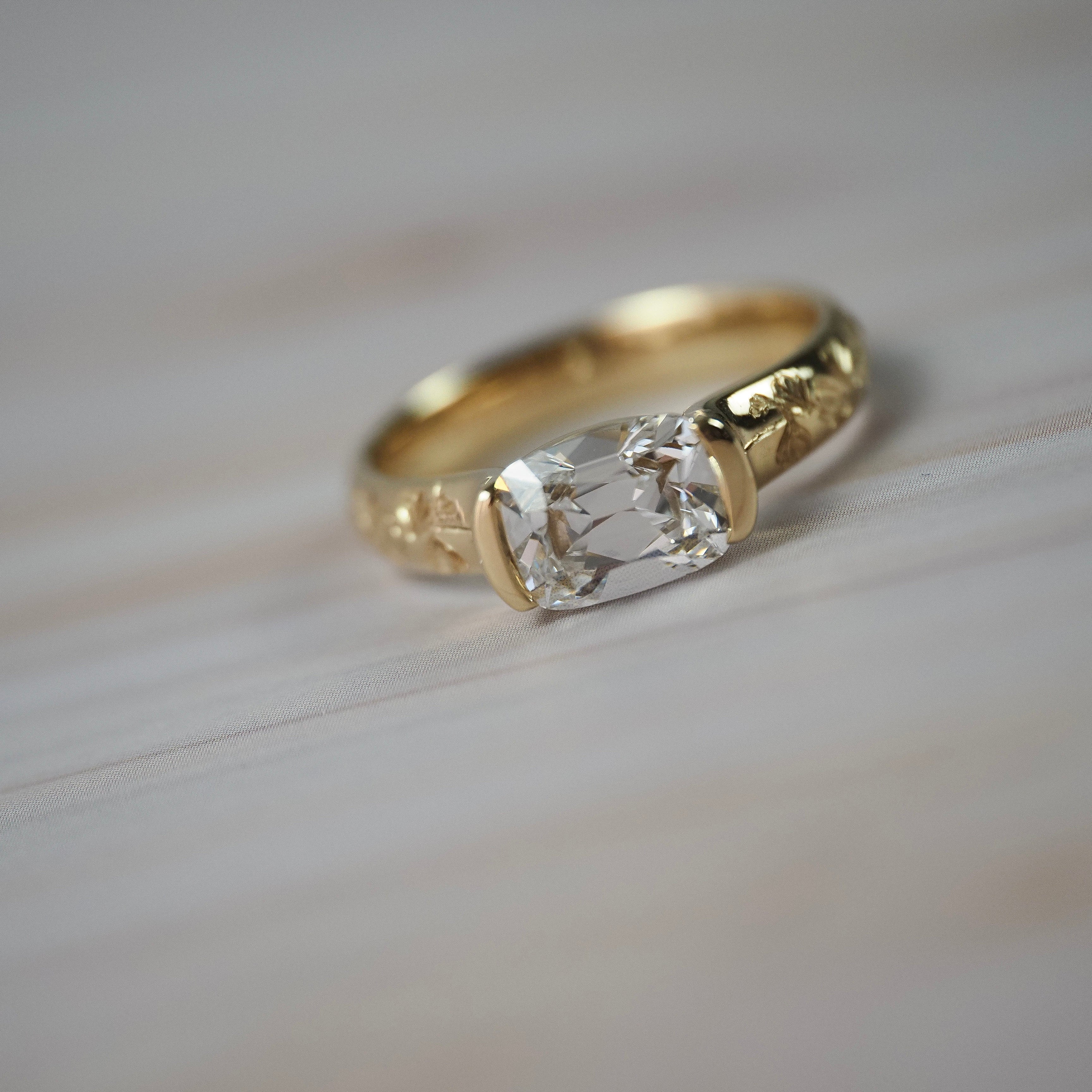 Magnolia hall-bezel solitaire featuring an elongated Old European cushion cut diamond with hand engraved magnolia flowers along the band.