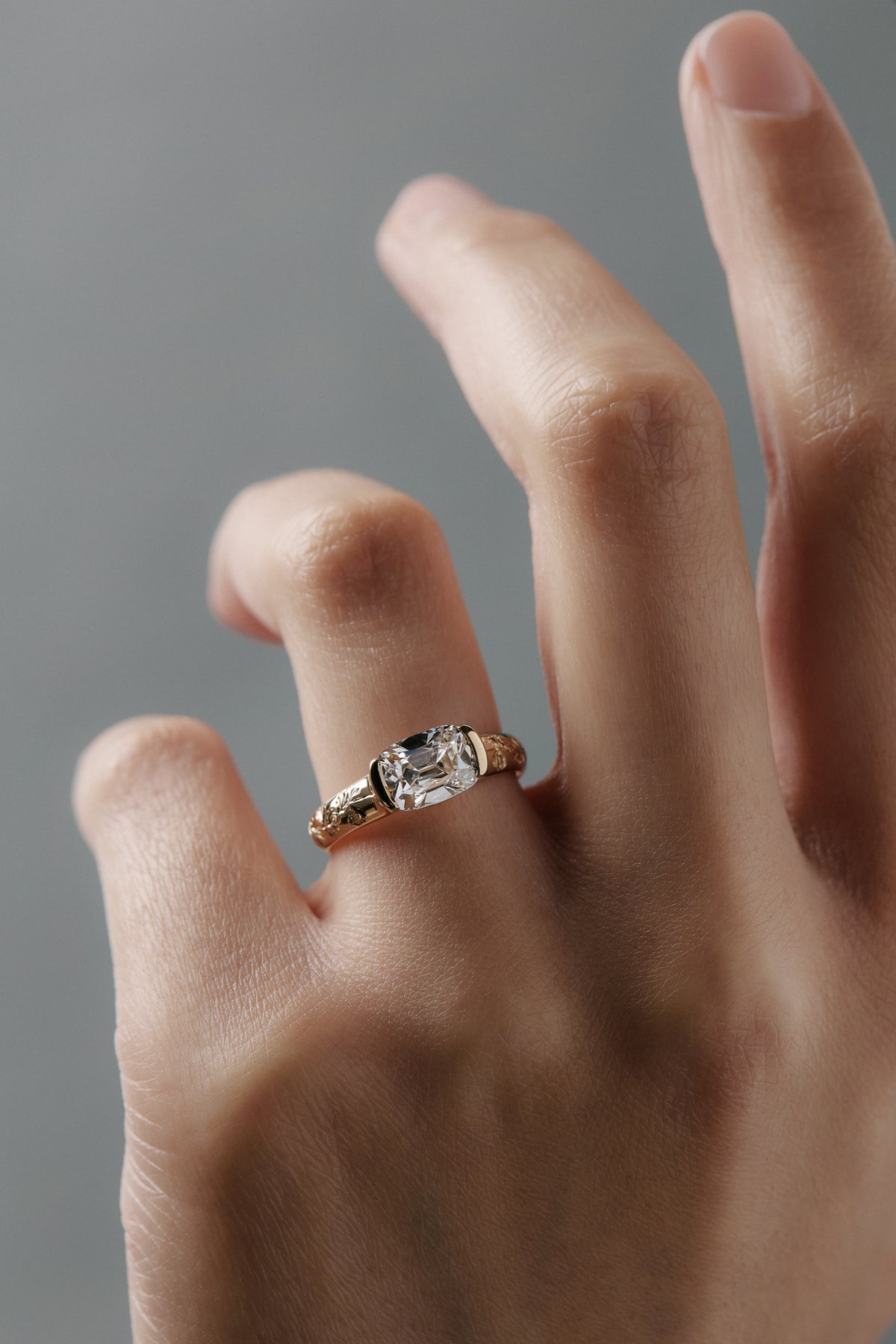Close-up of a woman wearing the Magnolia half bezel solitaire with an elongated Old European cushion cut diamond and hand engraved magnolia flowers.