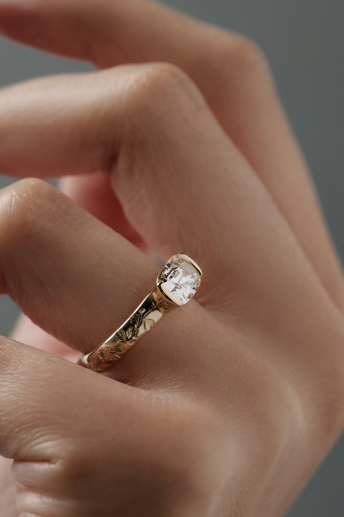 Close-up side view of the Magnolia half bezel solitaire on a woman's finger, highlighting  the hand engraved magnolia flowers and detailed diamond setting.
