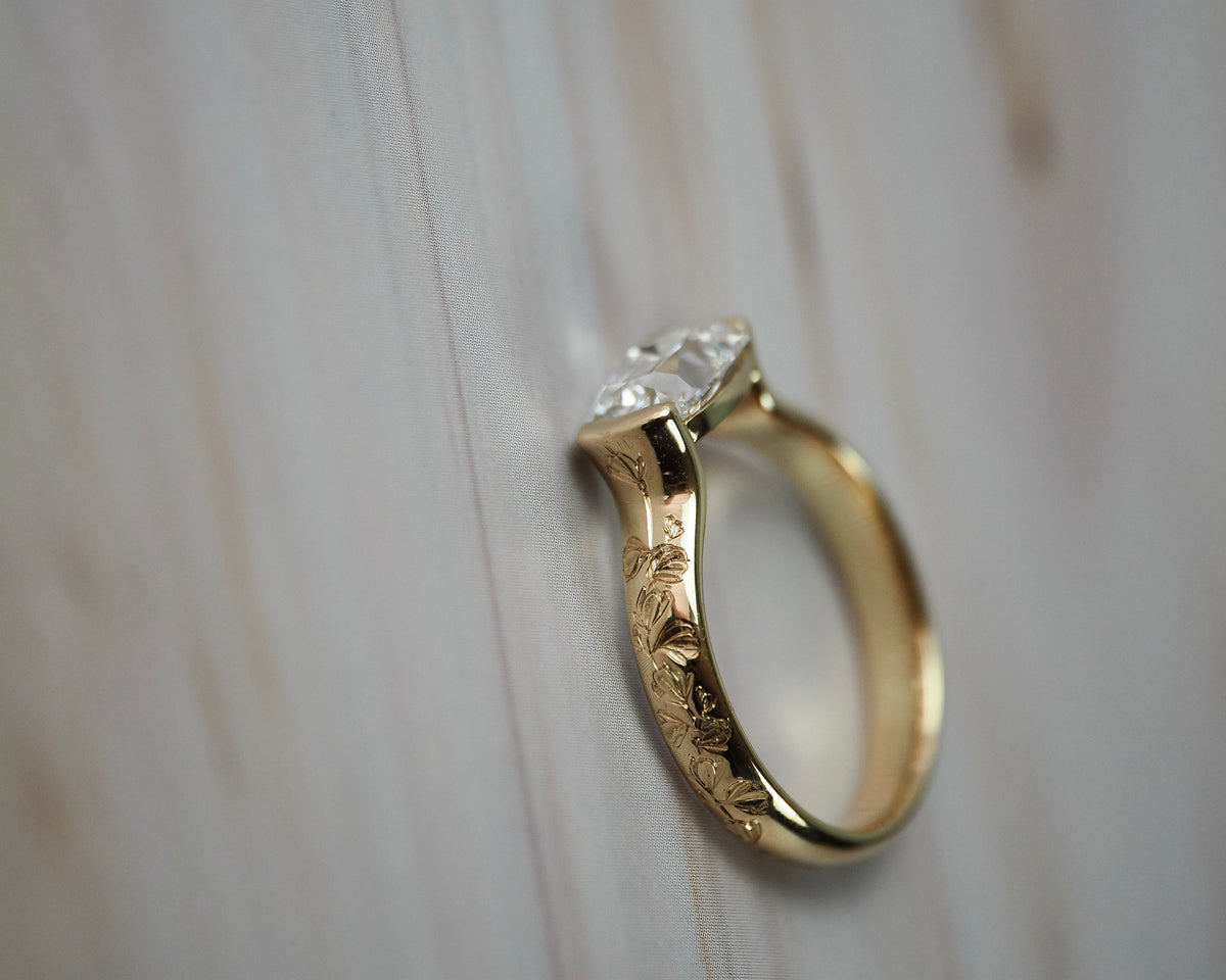 Close-up side view of the Magnolia half-bezel solitaire showing the detailed setting and hand engraved magnolia flowers along the band.