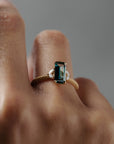Close-up of a woman wearing the Millie cluster solitaire, highlighting the rectangular teal sapphire, marquise diamonds- and intricate milgrained beaded band 