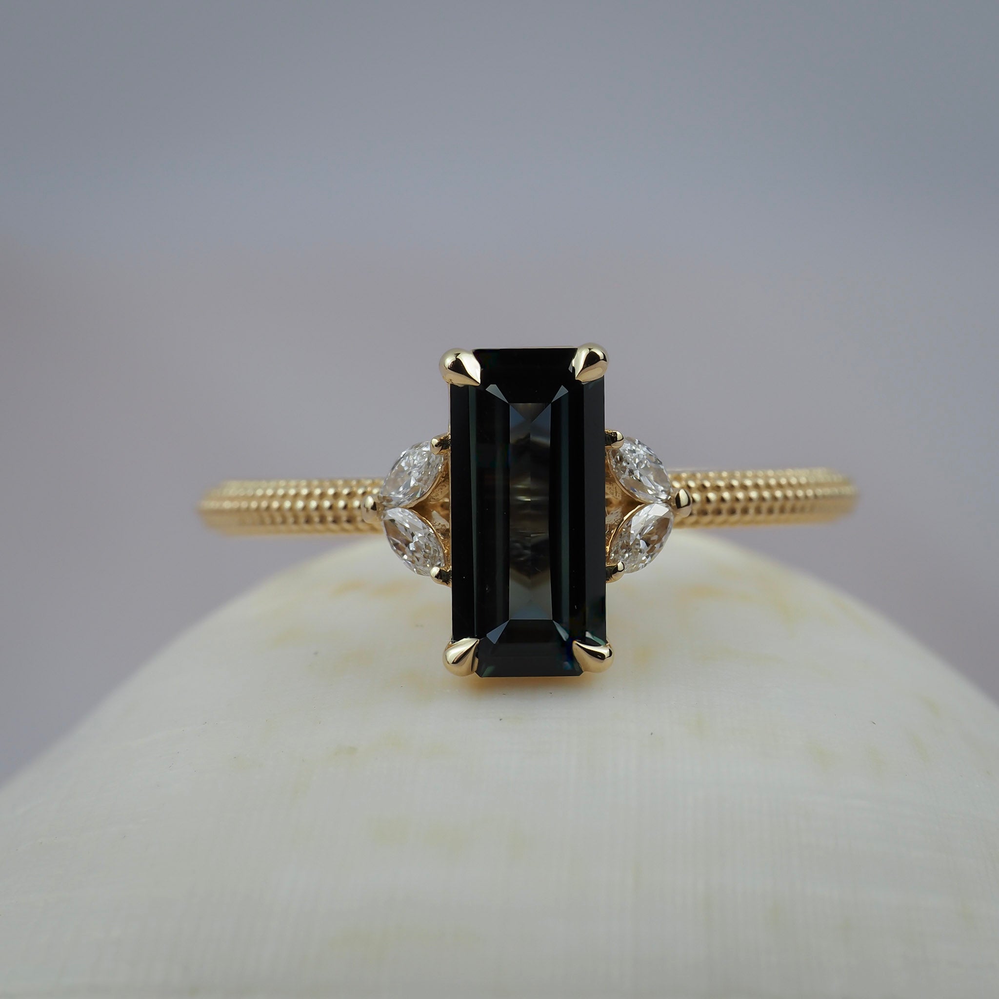 Millie cluster solitaire engagement featuring a rectangular lintel sapphire, marquise diamonds, and a migraines beaded gold band. 