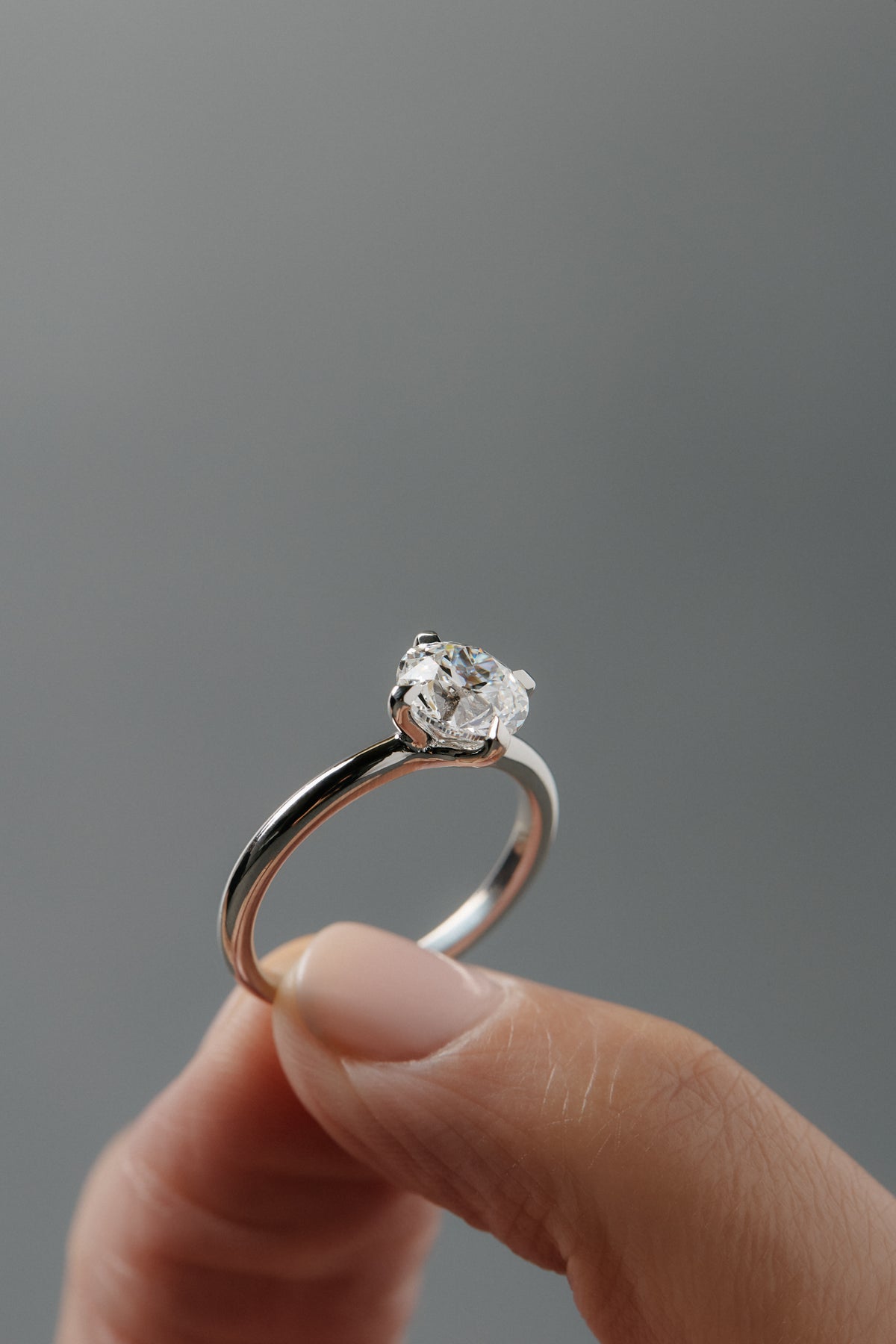 Close-up of women's fingers holding the Myra compass platinum claw solitaire with an Old European cut diamond.