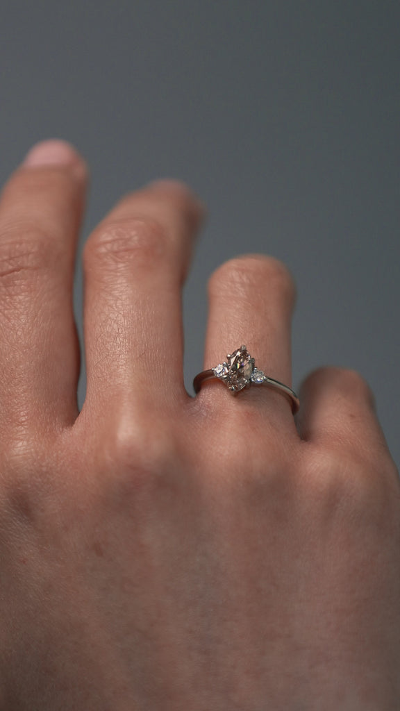Close-up video of a woman wearing the Rebecca three stone engagement ring, featuring a champagne toned moval cut diamond and white full cut diamonds. 