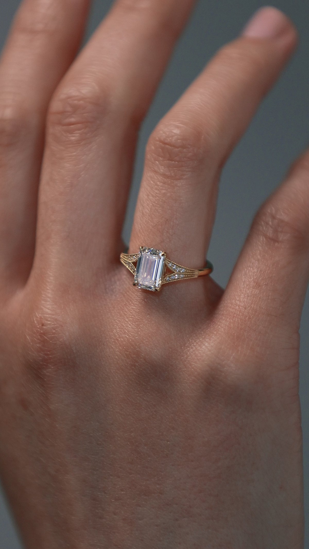 Close-up video of a woman wearing the Cora split-shank milgrain engagement solitaire with an emerald cut diamond and round accents. 