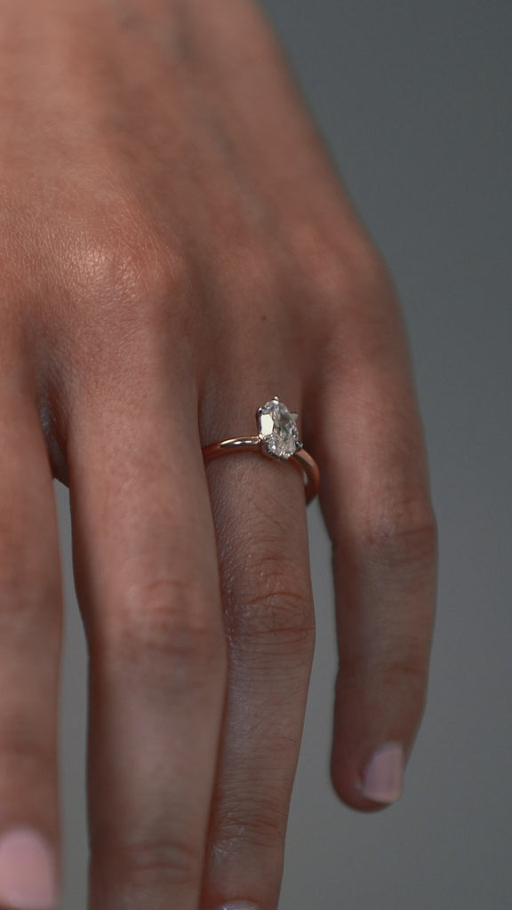 Close-up video of the lena six-claw solitaire engagement ring worn on a woman finger, featuring a moval shaped antique cut Old European diamond in a two-tone platinum and rose gold setting. 