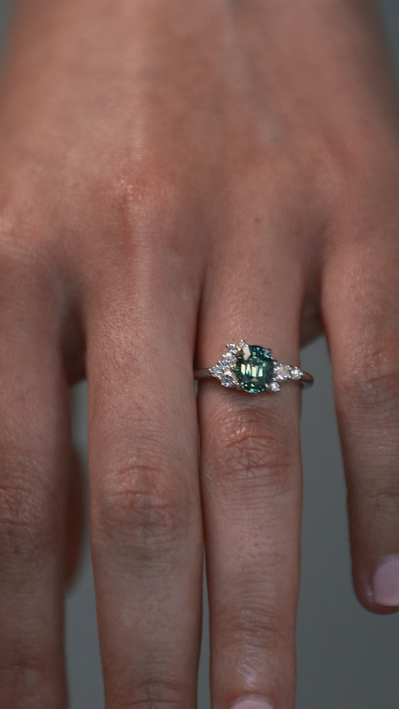 Close-up video of a woman wearing the Celeste teal sapphire and diamond cluster engagement ring on her finger. 