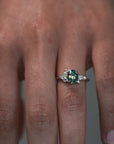 Close-up video of a woman wearing the Celeste teal sapphire and diamond cluster engagement ring on her finger. 