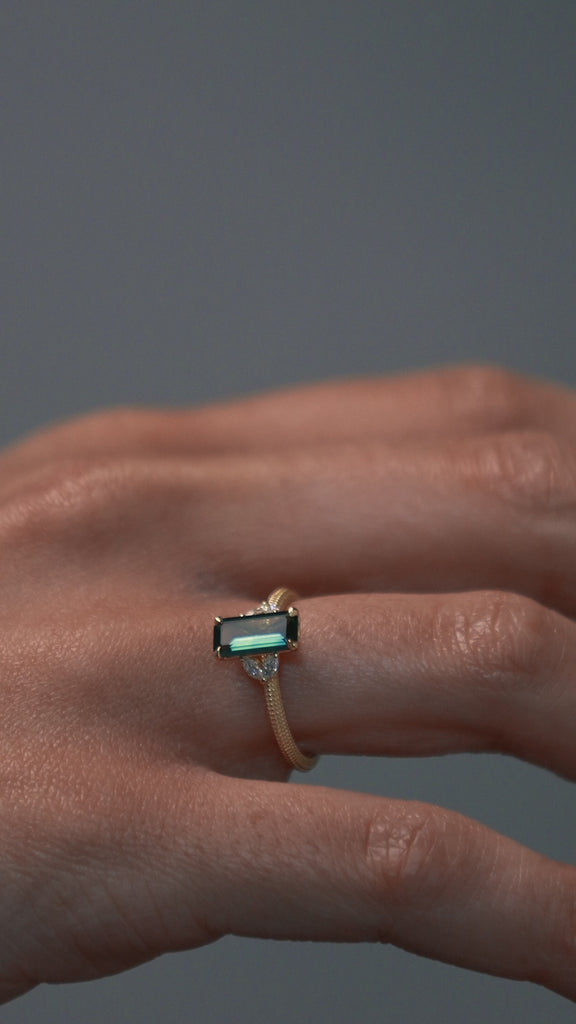 Close-up video of the Millie cluster solitaire engagement ring worn on a woman's hand, showcasing the rectangular teal sapphire, marquise diamonds, and milgrained beaded band.