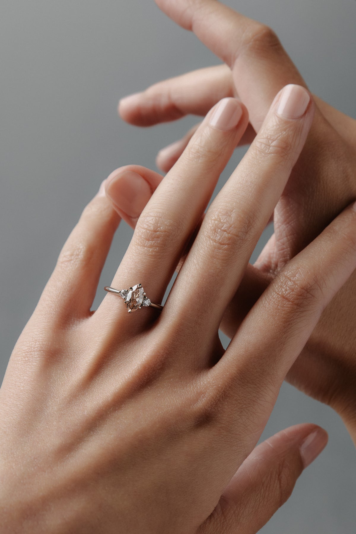 Stylized close-up of the Rebecca three stone engagement ring worn on a a woman's finger, featuring a champagne toned antique cut moval diamond and white full cut diamonds.