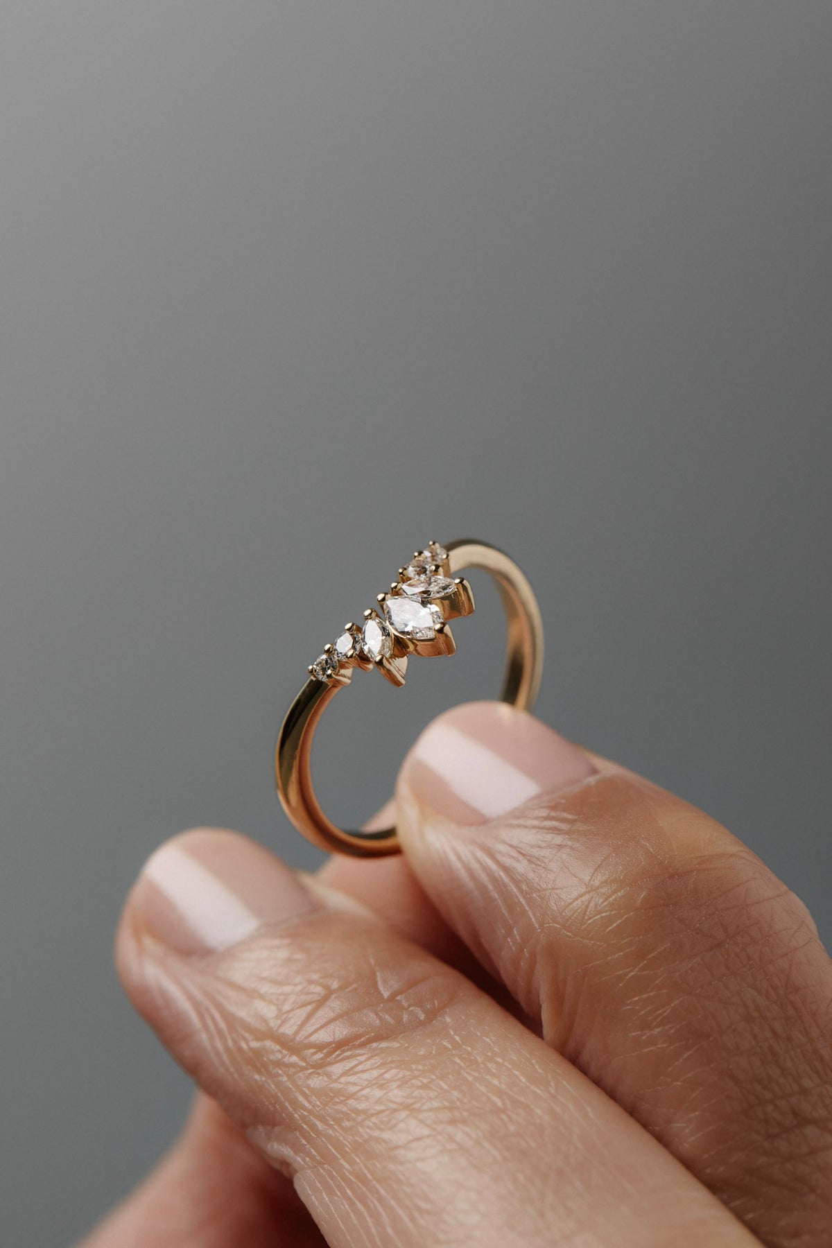 Close-up of a women's finger holding the Trillium curved gold wedding band, featuring marquise and round diamonds.