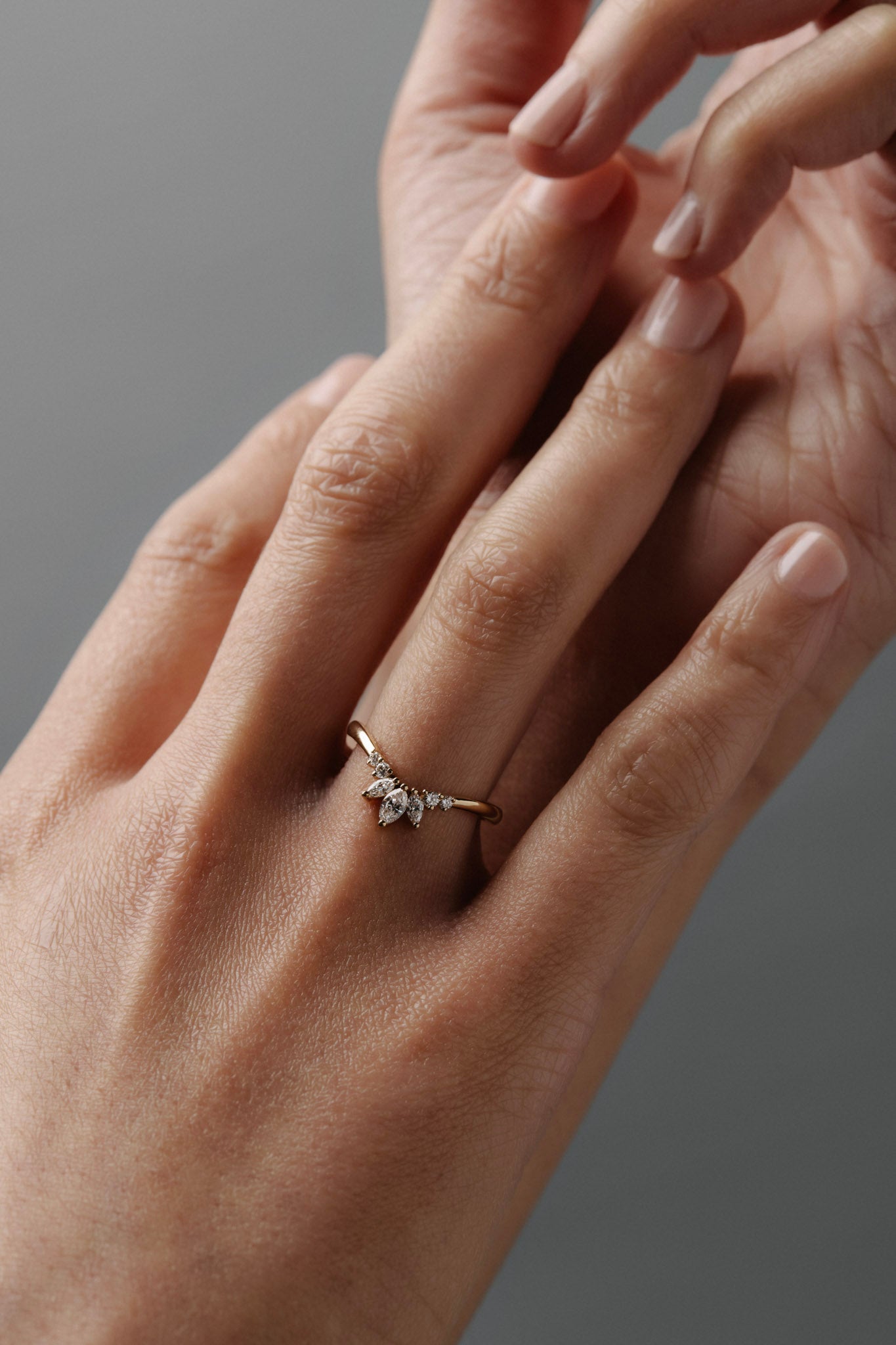 Close-up of a woman wearing the Trillium curved gold wedding band with marquise and round diamonds.