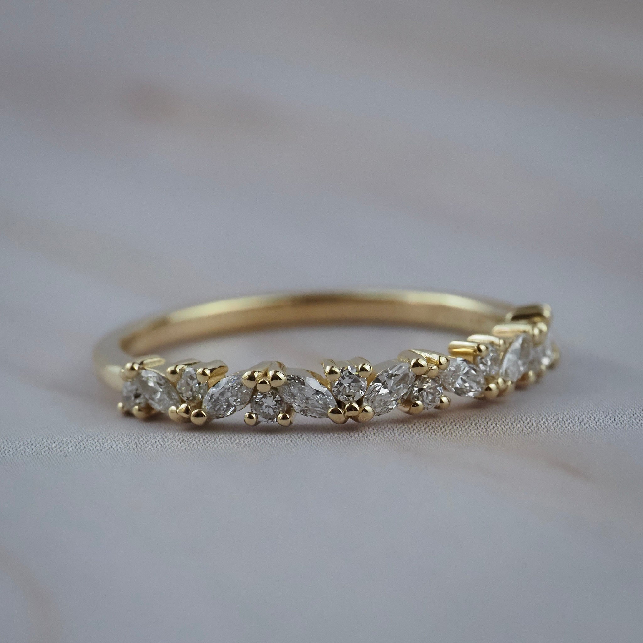 Marissa yellow gold wedding band featuring a row of marquise and round diamonds, photographed on a light gray marble surface.